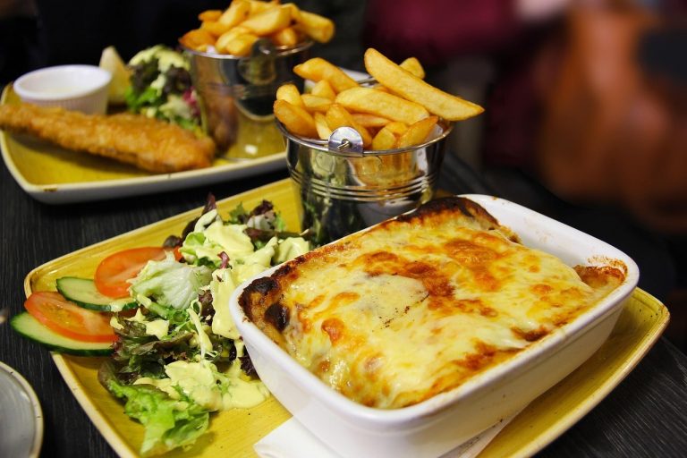 Hearty serving of homemade lasagna with golden chips, beautifully plated in a traditional Irish restaurant in Killarney, County Kerry. The lasagna features layers of rich beef ragu, creamy béchamel sauce, and melted cheese, paired with thick-cut crispy chips and a fresh side salad. Presented on a ceramic plate with a rustic wooden table backdrop, the meal blends Italian comfort food with classic Irish pub-style dining. A popular menu choice for visitors relaxing after sightseeing around Killarney National Park, Muckross House, and the Ring of Kerry. A warm, satisfying dish served in a friendly, welcoming Irish dining setting.